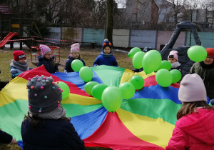 Dzieci maszerują z zielonymi balonami i żółtymi kwiatami, śpiewając piosenkę pt. Maszeruje wiosna